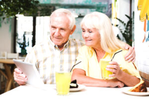 Old happy couple sitting in a cafe, smiling and looking at ipad